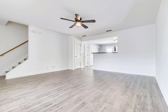 unfurnished living room with visible vents, baseboards, stairway, wood finished floors, and a ceiling fan