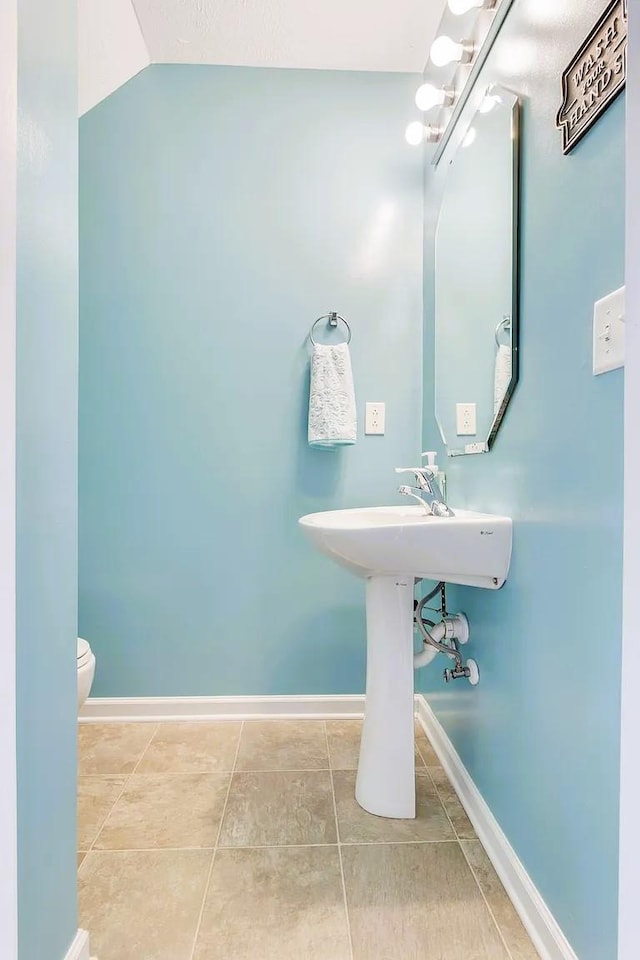 half bath with tile patterned floors, toilet, baseboards, and vaulted ceiling