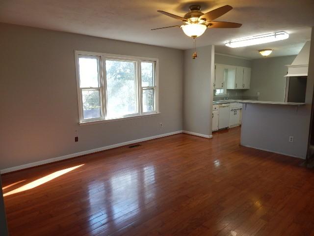 unfurnished living room with visible vents, baseboards, dark wood-type flooring, and ceiling fan