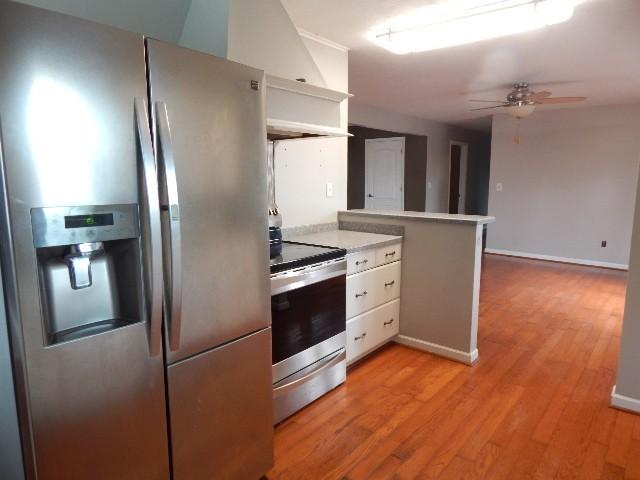 kitchen with light countertops, light wood-style flooring, a peninsula, stainless steel appliances, and a ceiling fan