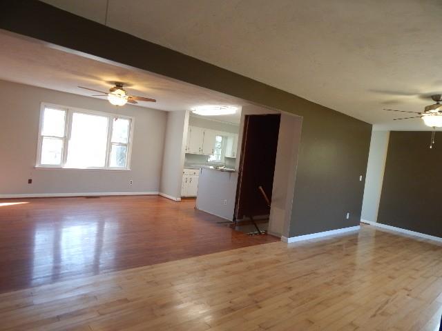 unfurnished living room featuring baseboards, wood finished floors, beam ceiling, and ceiling fan