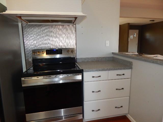 kitchen featuring under cabinet range hood, stainless steel electric range, and white cabinets