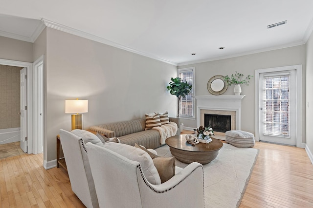 living room featuring light wood-type flooring, visible vents, ornamental molding, a high end fireplace, and baseboards