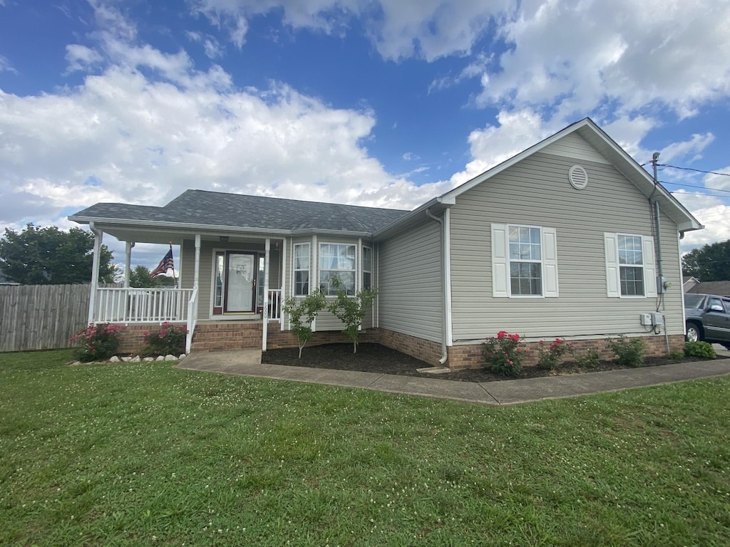 ranch-style house featuring covered porch, a shingled roof, a front lawn, and fence