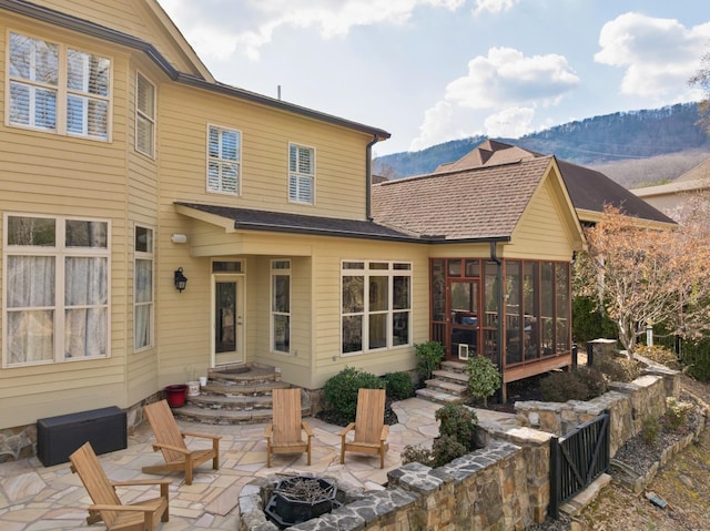 back of house with an outdoor fire pit, a mountain view, roof with shingles, a sunroom, and a patio area