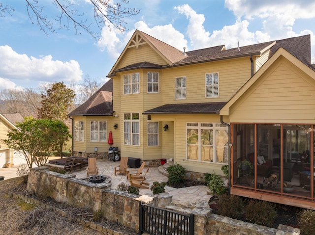 rear view of property with a patio, an outdoor fire pit, a shingled roof, and a sunroom