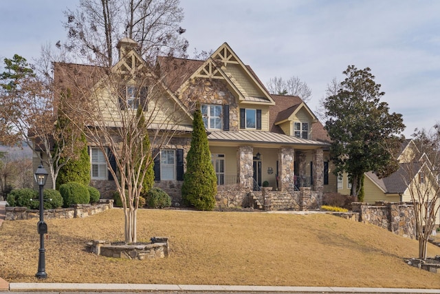 craftsman-style home featuring stone siding, a porch, a front yard, and a standing seam roof