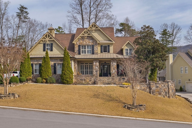 craftsman-style house featuring a front lawn, a standing seam roof, stone siding, metal roof, and a chimney