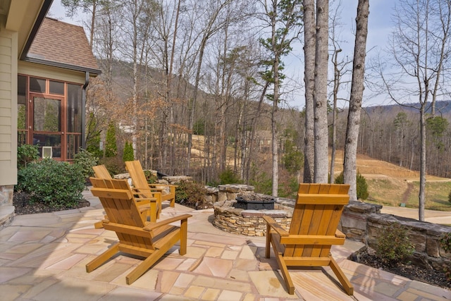 view of patio / terrace with an outdoor fire pit, a forest view, and a sunroom