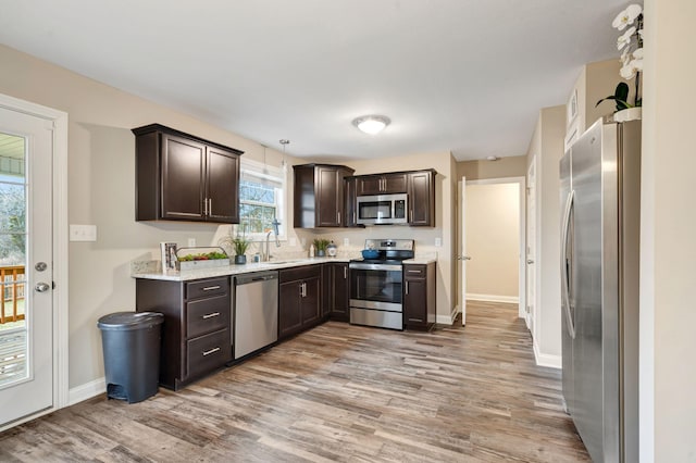 kitchen with light wood-type flooring, a sink, stainless steel appliances, baseboards, and dark brown cabinets