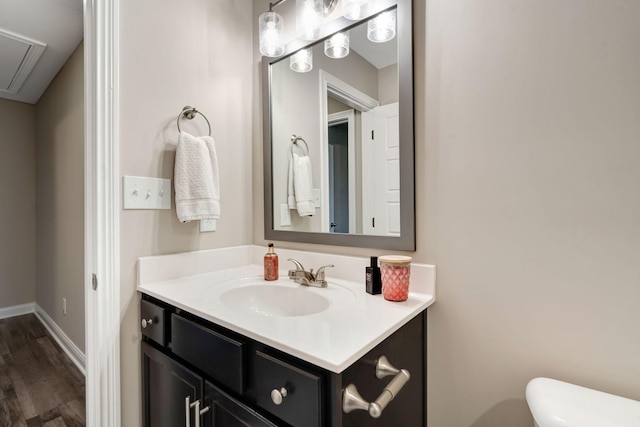 half bathroom featuring vanity, toilet, wood finished floors, and baseboards