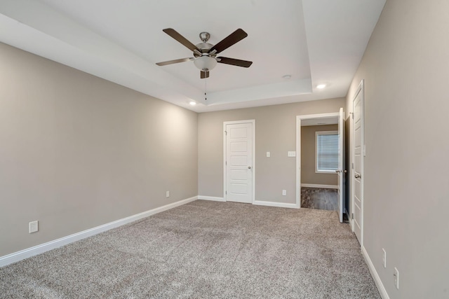 unfurnished bedroom featuring carpet flooring, ceiling fan, baseboards, and a tray ceiling