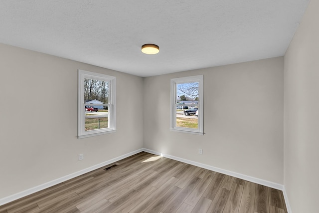 unfurnished room featuring a textured ceiling, wood finished floors, visible vents, and baseboards