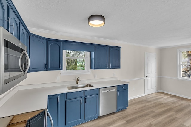 kitchen with blue cabinets, a sink, appliances with stainless steel finishes, crown molding, and light wood finished floors