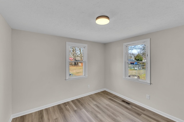 empty room with visible vents, baseboards, light wood-style floors, and a textured ceiling