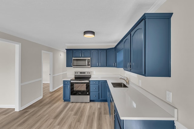 kitchen featuring light wood-style flooring, blue cabinetry, a sink, appliances with stainless steel finishes, and light countertops