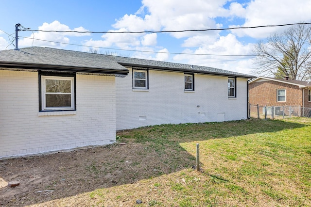 back of house with brick siding, a shingled roof, fence, a yard, and crawl space