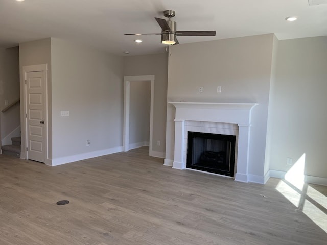 unfurnished living room featuring baseboards, ceiling fan, a tiled fireplace, and light wood finished floors