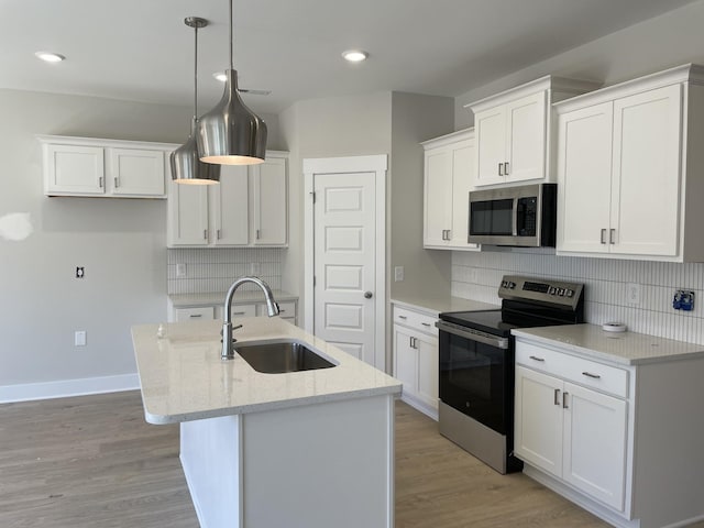 kitchen featuring a center island with sink, a sink, stainless steel appliances, light wood-style floors, and white cabinetry