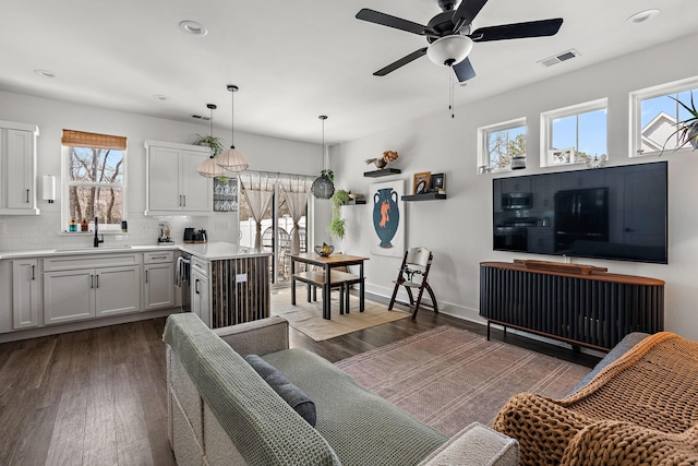 living room featuring dark wood-type flooring, a ceiling fan, visible vents, and baseboards