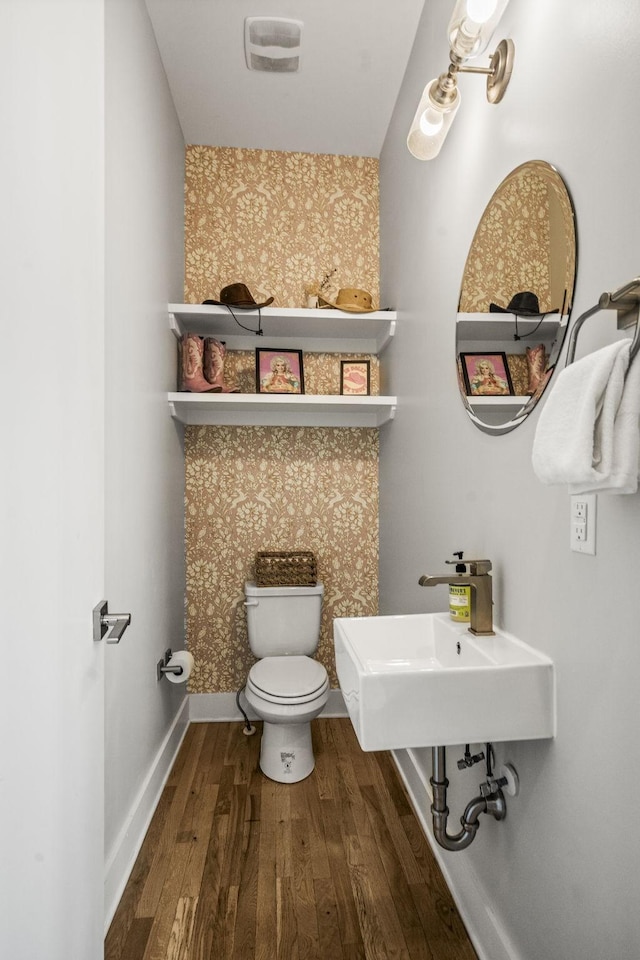 half bathroom with visible vents, wallpapered walls, baseboards, toilet, and wood finished floors