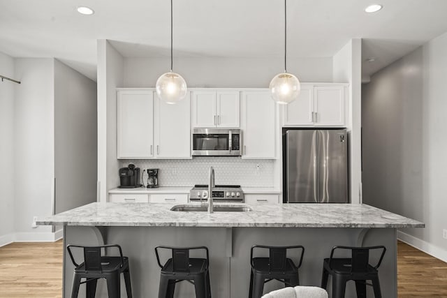 kitchen featuring stainless steel appliances, light wood-style floors, white cabinetry, a kitchen breakfast bar, and backsplash