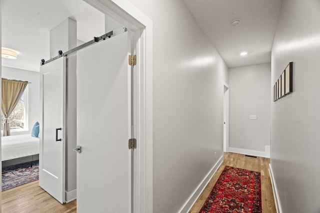 corridor with a barn door, baseboards, and light wood-style floors