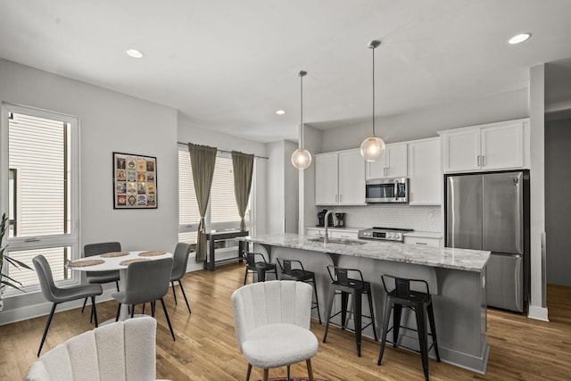 kitchen with tasteful backsplash, an island with sink, stainless steel appliances, white cabinetry, and a sink