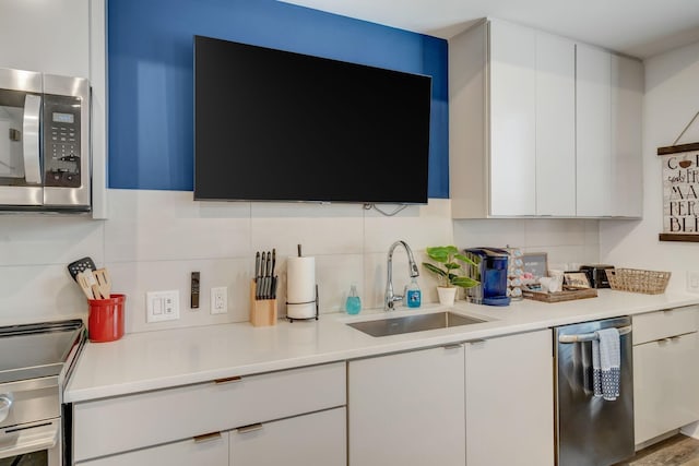 kitchen featuring a sink, decorative backsplash, light countertops, stainless steel appliances, and white cabinetry