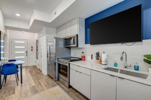 kitchen featuring backsplash, light countertops, white cabinets, stainless steel appliances, and a sink