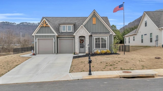 view of front facade featuring board and batten siding, a shingled roof, fence, stone siding, and driveway