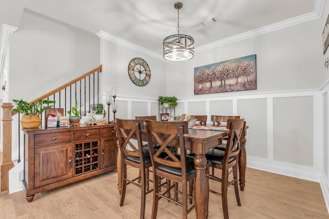 dining area with light wood-type flooring, visible vents, crown molding, a decorative wall, and a chandelier