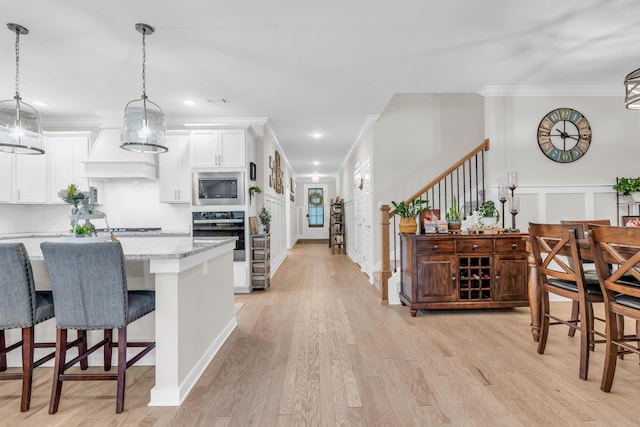 kitchen with stainless steel microwave, oven, a breakfast bar, custom exhaust hood, and white cabinetry