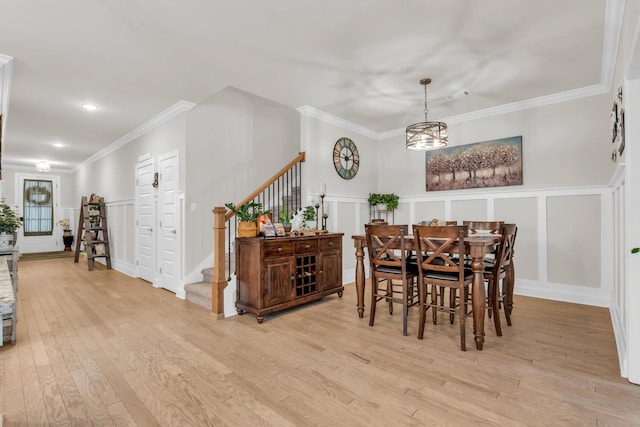 dining room with light wood finished floors, stairway, crown molding, and a decorative wall