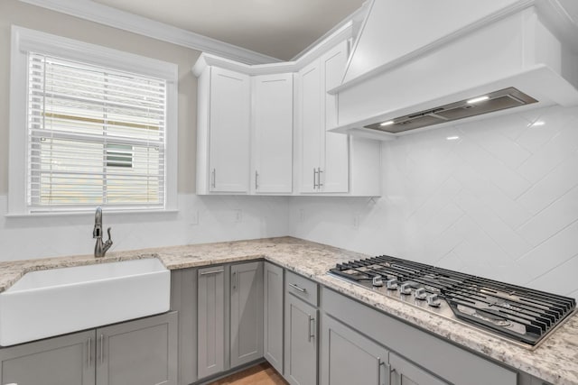 kitchen featuring custom exhaust hood, gray cabinets, ornamental molding, a sink, and stainless steel gas stovetop