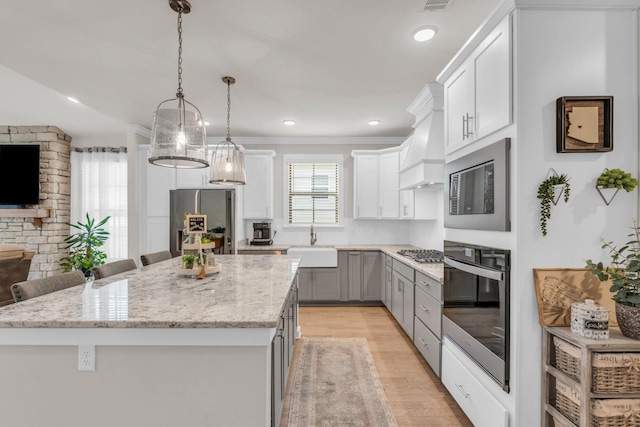 kitchen featuring light wood-type flooring, a sink, a kitchen island, appliances with stainless steel finishes, and crown molding