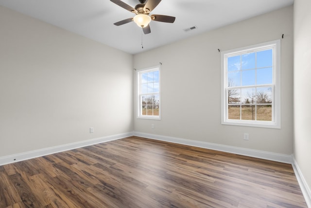 empty room with dark wood-type flooring, a ceiling fan, visible vents, and baseboards