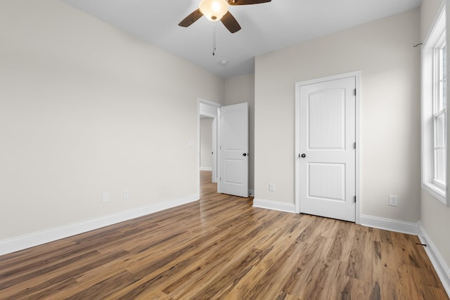 unfurnished bedroom with a ceiling fan, multiple windows, wood finished floors, and baseboards