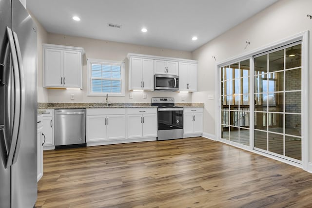 kitchen featuring wood finished floors, recessed lighting, stainless steel appliances, white cabinets, and light stone countertops