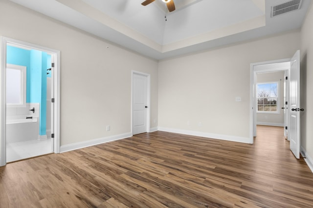 unfurnished bedroom featuring visible vents, a tray ceiling, wood finished floors, connected bathroom, and baseboards