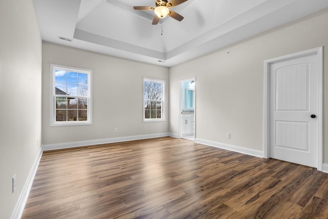 spare room with visible vents, a tray ceiling, wood finished floors, baseboards, and ceiling fan