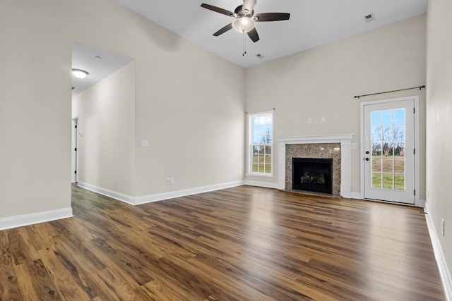 unfurnished living room featuring visible vents, dark wood-type flooring, a premium fireplace, baseboards, and ceiling fan