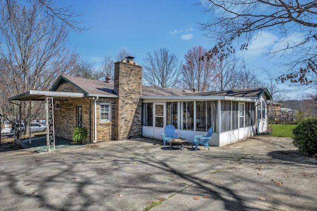 rear view of house featuring brick siding, a fire pit, a chimney, a sunroom, and a patio