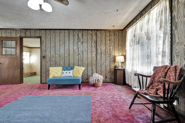 sitting room with crown molding, wooden walls, a ceiling fan, and carpet floors