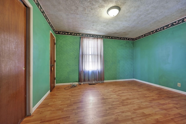 unfurnished room featuring visible vents, a textured ceiling, baseboards, and wood finished floors