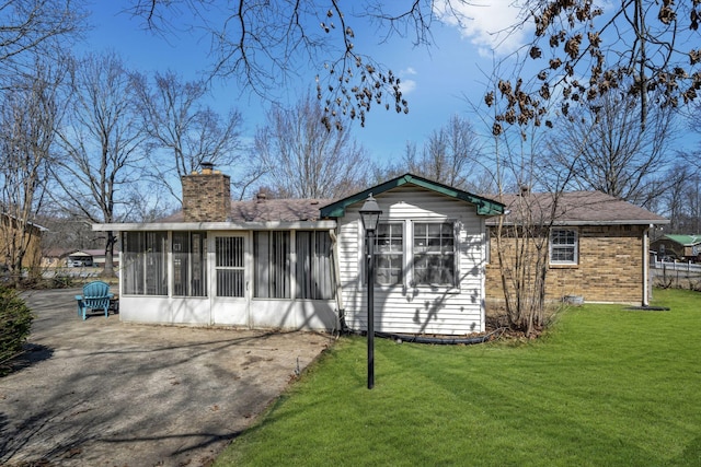 view of front facade with brick siding, a front lawn, roof with shingles, a chimney, and a sunroom