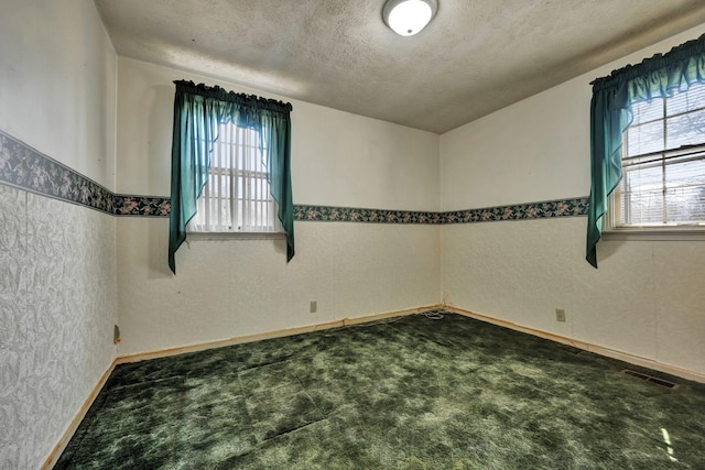 carpeted empty room with a textured wall, visible vents, and a textured ceiling