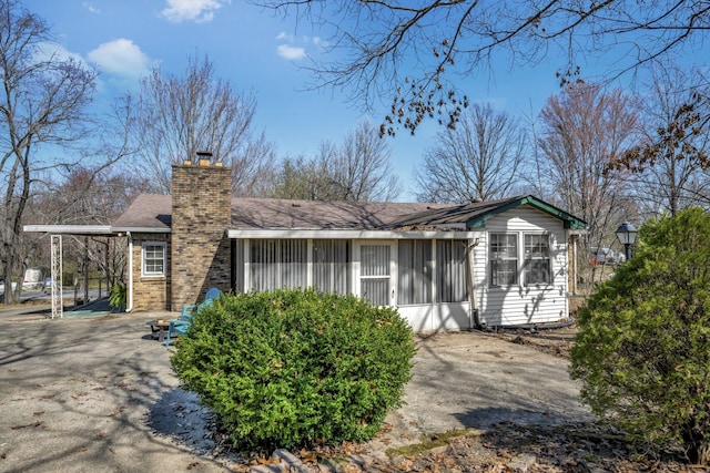 view of side of home with a carport, a chimney, and a sunroom