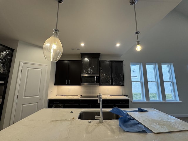 kitchen with dark cabinetry, stainless steel microwave, backsplash, and a sink