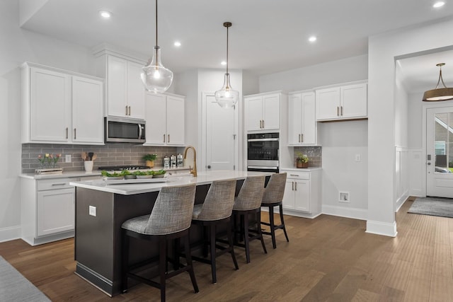 kitchen featuring a center island with sink, dark wood finished floors, light countertops, white cabinetry, and stainless steel microwave